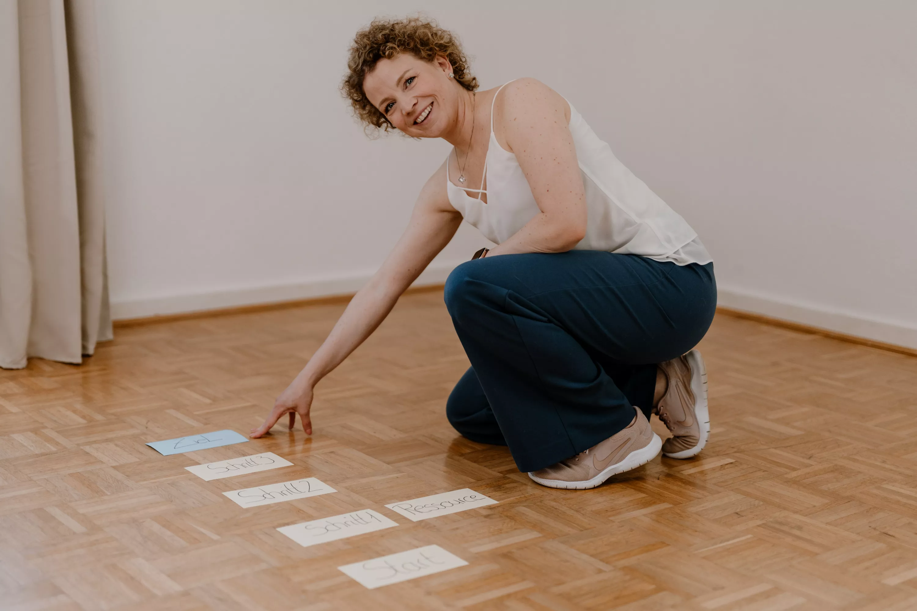 Carina Häbel zeigt auf eine Karte, es liegen mehrere Karten auf dem Boden. Sie lacht und zeigt deutliches Interesse am gegenüber. Sie befindet sich in einer Coaching-Session, bzw. psychologischen Beratung.