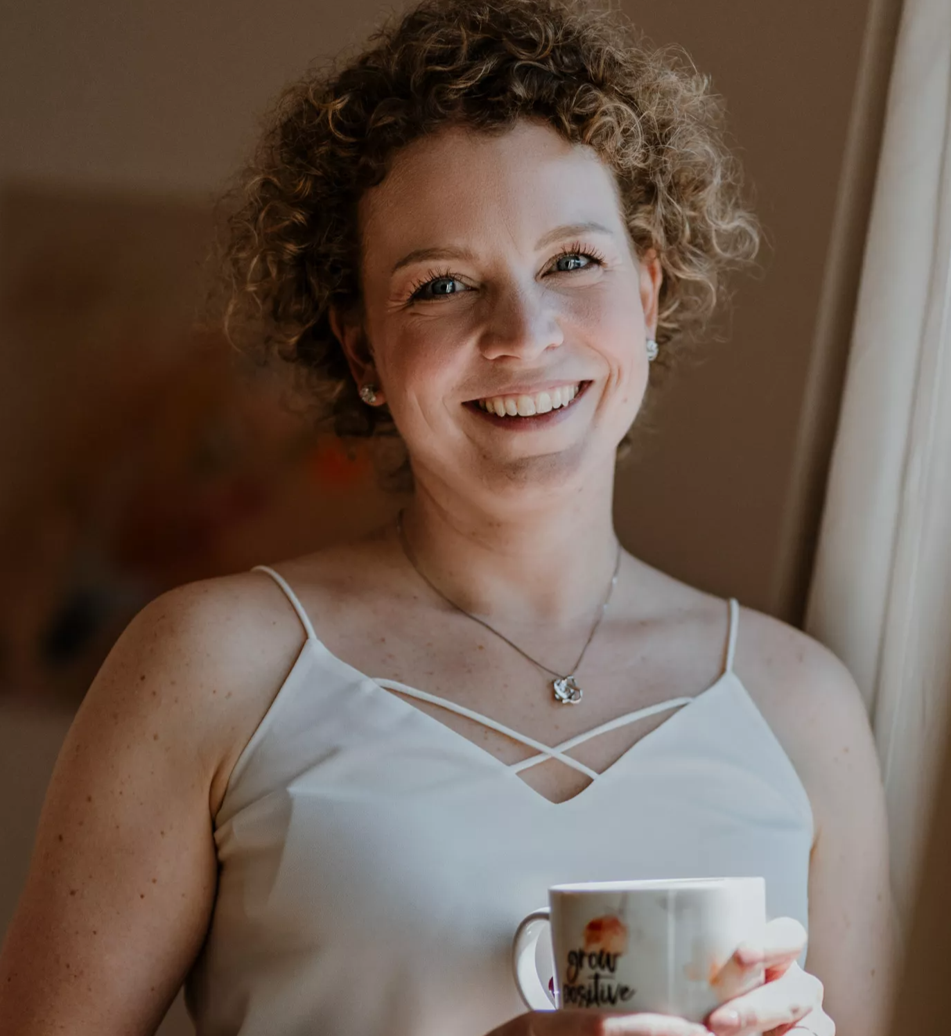 Carina hält eine Tasse in der Hand und strahlt dich an